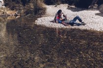 Вид збоку молода пара лежить на гірському узбережжі гірської річки біля скелі — стокове фото