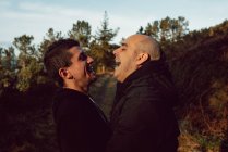Laughing homosexual couple hugging on path in forest in sunny day — Stock Photo
