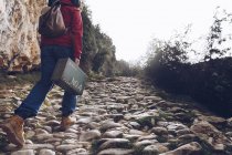 Back view of casual woman carrying case and walking on rocks of clear stream of water in nature — Stock Photo