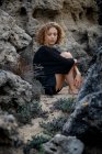 Joven mujer pensativa sentada en las rocas y abrazando las rodillas - foto de stock