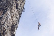 Von unten des Bergsteigers hängt am Seil an rauer Klippe gegen blauen Himmel — Stockfoto