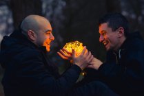 Casal homossexual com luzes de fadas iluminadas sentado na floresta escura à noite — Fotografia de Stock