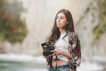 Thoughtful young woman holding camera on sea coast — Stock Photo