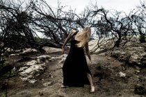 Jovem bailarina em preto desgaste dançando em terra entre madeiras secas — Fotografia de Stock