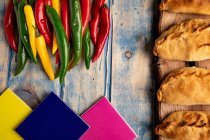 Rissóis cozidos em casa e pimentas verdes e vermelhas frescas na mesa de madeira cinza com azulejos coloridos — Fotografia de Stock
