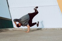 Guy performing handstand while dancing near wall of modern building on city street — Stock Photo