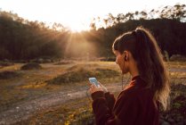 Молодая хипстерша с пирсингом и наушниками слушает музыку с мобильного телефона в сельской местности — стоковое фото