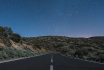 Vue pittoresque de la route asphaltée entre les collines et le ciel avec des étoiles la nuit à Tenerife, Îles Canaries, Espagne — Photo de stock
