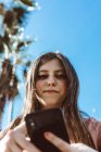Chica adolescente mirando su teléfono inteligente en la calle en un día soleado - foto de stock