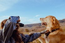 Side view of young woman shooting on camera funny dog between meadow and blue sky — Stock Photo