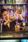 Femme attrayante verser divers liquides dans le verre tout en préparant un cocktail derrière le comptoir dans le bar — Photo de stock