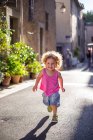 Happy funny girl running on asphalt street between buildings in summer — Stock Photo