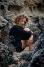 Jeune femme réfléchie assise dans des rochers et embrassant les genoux — Photo de stock
