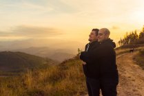 Щасливого гомосексуального пару обіймаючи і насолоджуючись заходом сонця на маршруті в горах — стокове фото