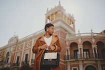 Fiduciosa donna afroamericana elegante in giacca in possesso di borsa e in posa sulla strada — Foto stock