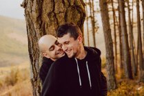 Allegra coppia omosessuale che abbraccia vicino albero nella foresta e pittoresca vista sulla valle — Foto stock