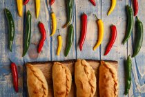 Hausgemachte gebackene Pasteten und frische grüne und rote Chilischoten auf grauem Holztisch — Stockfoto
