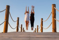 Молоді балерини в чорно-білому одязі з посиленими руками в повітрі на пішохідному мосту і блакитним небом в сонячний день — стокове фото