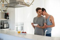 Ласковая гей-пара, которая завтракает и обнимается дома на кухне — стоковое фото