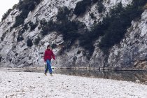 Lässige Frau trägt Koffer und geht am Ufer des klaren Wasserflusses in der Natur spazieren — Stockfoto