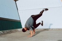Guy performing handstand while dancing near wall of modern building on city street — Stock Photo
