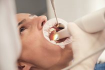 Die Hand des Zahnarztes in Handschuhen und Maske mit modernen Geräten für die Zähne der Patientin in der Zahnarztpraxis — Stockfoto