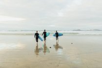 Personas con tabla de surf caminando cerca del mar - foto de stock