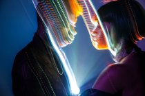 Traces lumineuses de lumière colorée sur les visages de jeune homme et femme sur fond bleu — Photo de stock