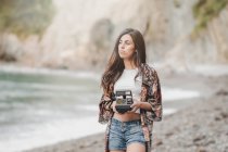 Thoughtful young woman holding camera on sea coast — Stock Photo