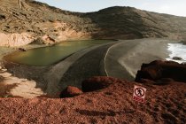 Piccolo segno di cautela posizionato vicino a un piccolo lago una ruvida collina rocciosa nella giornata di sole in campagna — Foto stock