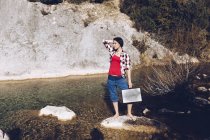 Donna in piedi su roccia con caso vicino acqua limpida nel lago — Foto stock