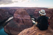 Vista trasera de un tipo barbudo con mochila mirando un hermoso cañón y un río tranquilo en un día soleado en la costa oeste de Estados Unidos - foto de stock