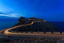 Lange Belichtung von Lichtpfaden bei Nacht mit Leuchtturm auf Hügel — Stockfoto
