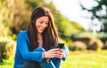 Портрет молодой женщины, сидящей на траве на смартфоне — стоковое фото