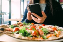 Mulher de colheita usando telefone celular e sentado à mesa com deliciosa salada no café — Fotografia de Stock