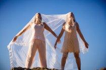 From below young mysterious women with upped hands holding white textile and posing on rocks and blue sky — Stock Photo