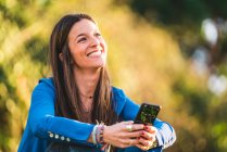 Портрет молодої жінки за допомогою смартфона, що сидить на траві в парі — стокове фото