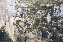 Von unten des Bergsteigers hängt am Seil an rauer Klippe gegen blauen Himmel — Stockfoto