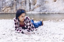Молода жінка лежить на гірському узбережжі гірської річки біля скелі — стокове фото
