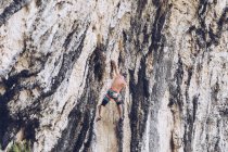 Вид збоку на невпізнаваного чоловіка в шортах, що піднімаються вгору по скелі в сонячний день в сільській місцевості — стокове фото
