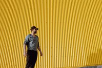 Barbu gars en tenue tendance debout contre le mur jaune de bâtiment moderne par jour ensoleillé sur la rue de la ville — Photo de stock