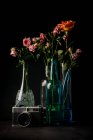 Vintage photo camera and glass vases with bouquets of lovely flowers on black background — Stock Photo