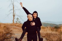 Happy homosexual couple having fun on route between plants in mountains — Stock Photo