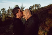 Feliz pareja homosexual abrazándose en el bosque en un día soleado - foto de stock