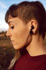Primer plano de la joven hipster con piercing y auriculares escuchando música en el campo - foto de stock
