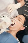 Die Hand des Zahnarztes in Handschuhen und Maske mit modernen Geräten für die Zähne der Patientin in der Zahnarztpraxis — Stockfoto