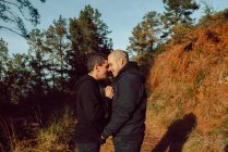Heureux couple homosexuel étreignant et embrassant sur le chemin dans la forêt dans la journée ensoleillée — Photo de stock