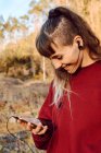 Jovem hipster mulher com piercing e fones de ouvido ouvir música com telefone celular no campo — Fotografia de Stock