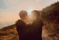 Pareja homosexual romántica abrazándose en el camino en las montañas en la luz del sol brillante al atardecer - foto de stock