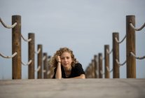 Junge Frau liegt auf Holzsteg in der Natur und blickt in Kamera — Stockfoto